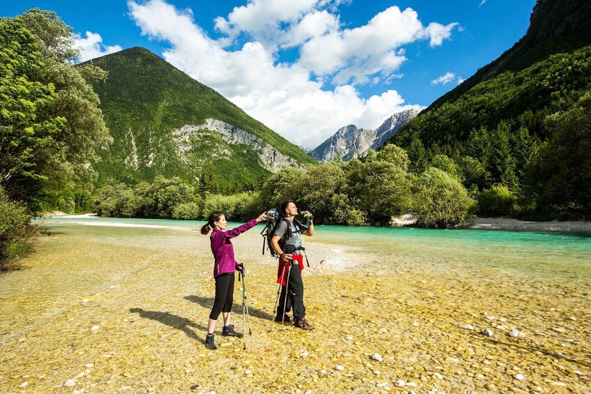 Two people hiking in a mountainous area with clear water and lush greenery. 1