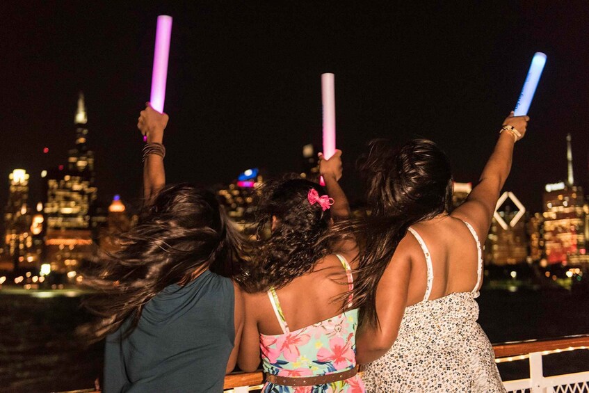 Tres personas sosteniendo palitos luminosos, con un paisaje urbano de fondo. 2