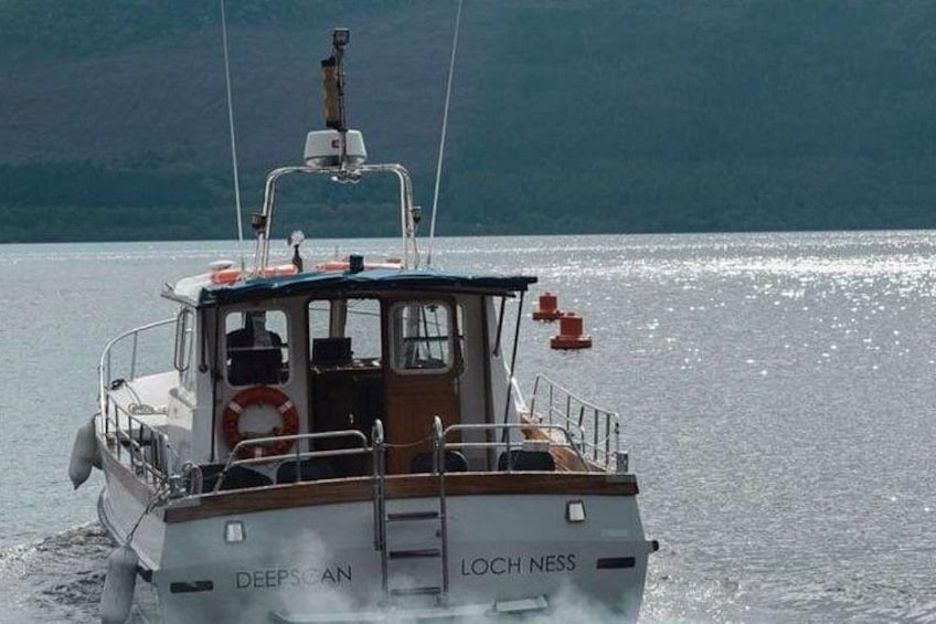 A boat named 'DEEPSCAN LOCHNESS' on water with a forested hill in the background. 5