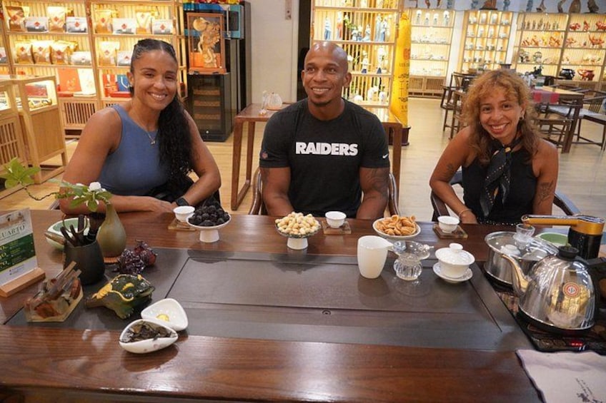 A group of people seated at a wooden table with various food items and drinks. 2
