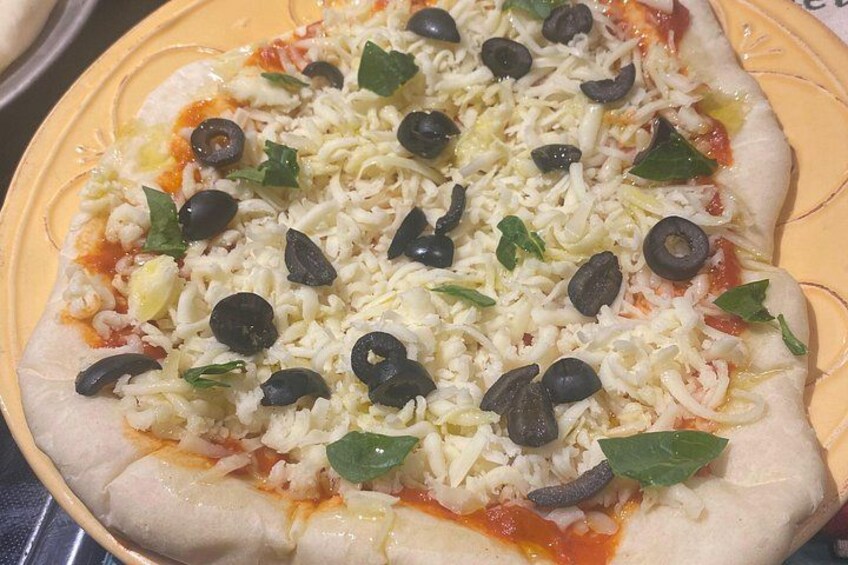 Pizza met kaas, zwarte olijven en groene blaadjes op een geel bord. 3