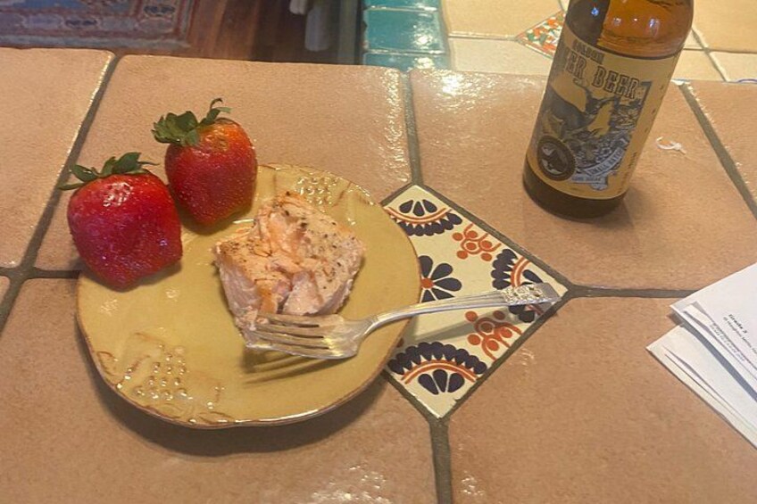 Een bord met een stuk zalm, twee aardbeien en een fles bier op een betegelde tafel. 2
