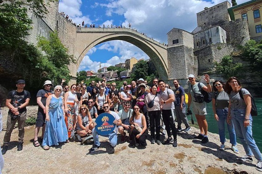Un grupo de personas posando frente a un puente de piedra con un castillo al fondo. 3
