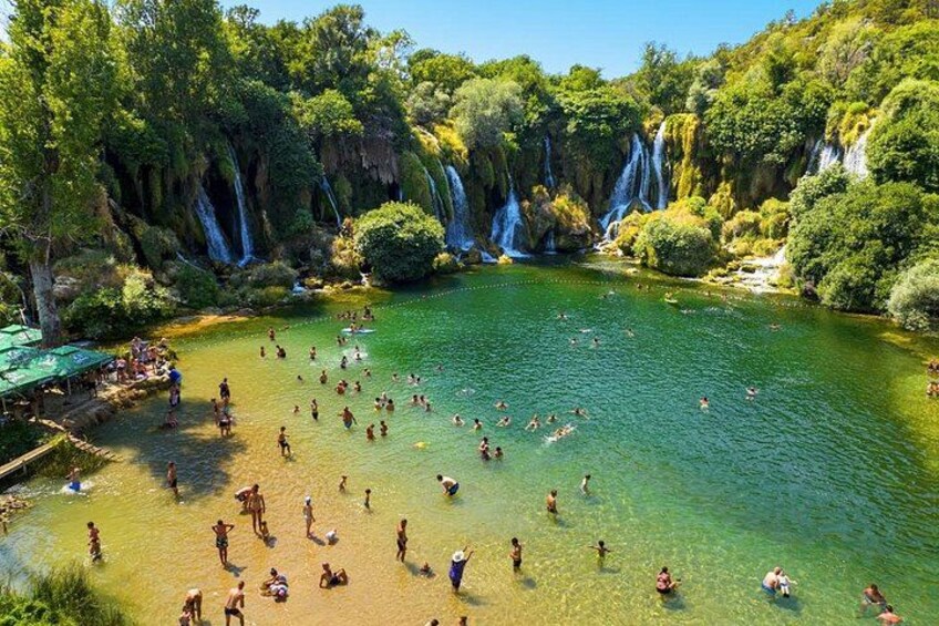 Paisaje natural con una cascada, agua cristalina y gente nadando. 5
