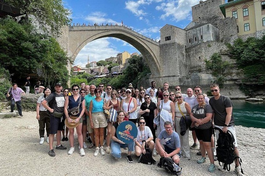 A group of people posing in front of a stone bridge with a castle in the background. 2