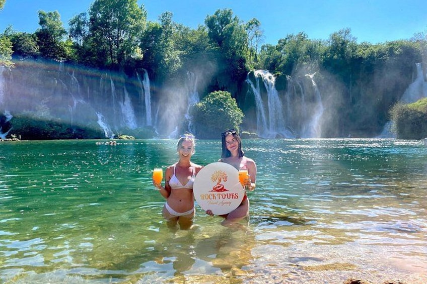 Dos personas en un cuerpo de agua cristalina con cascadas al fondo. 2