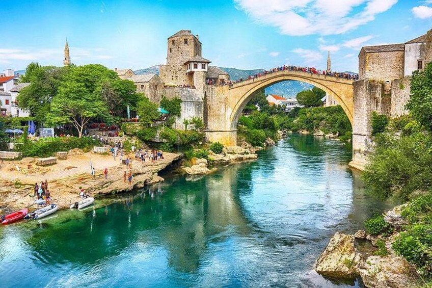 Un puente de piedra histórico sobre un río, rodeado de exuberante vegetación y edificios antiguos. 1