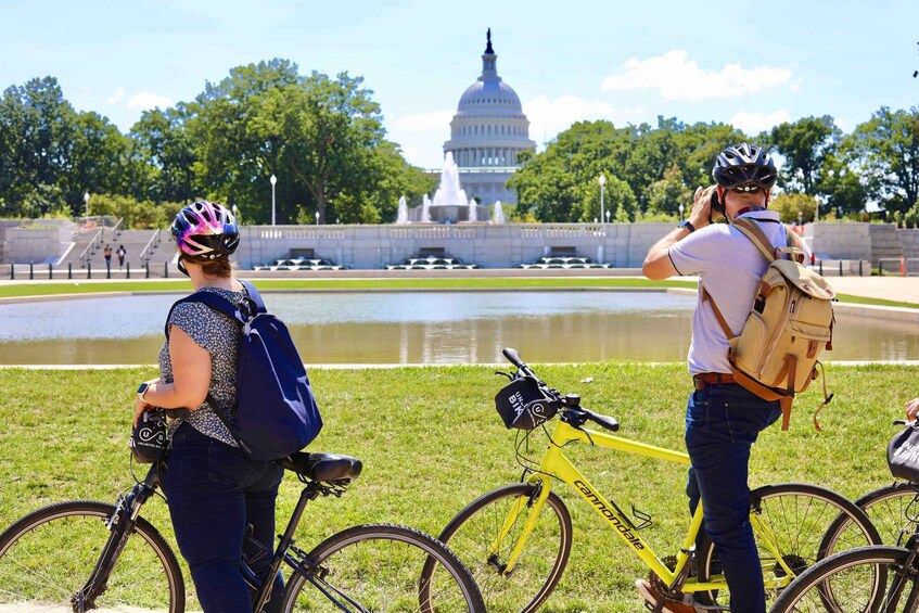 Dos personas en bicicleta cerca de una fuente, con el edificio del Capitolio al fondo. 4