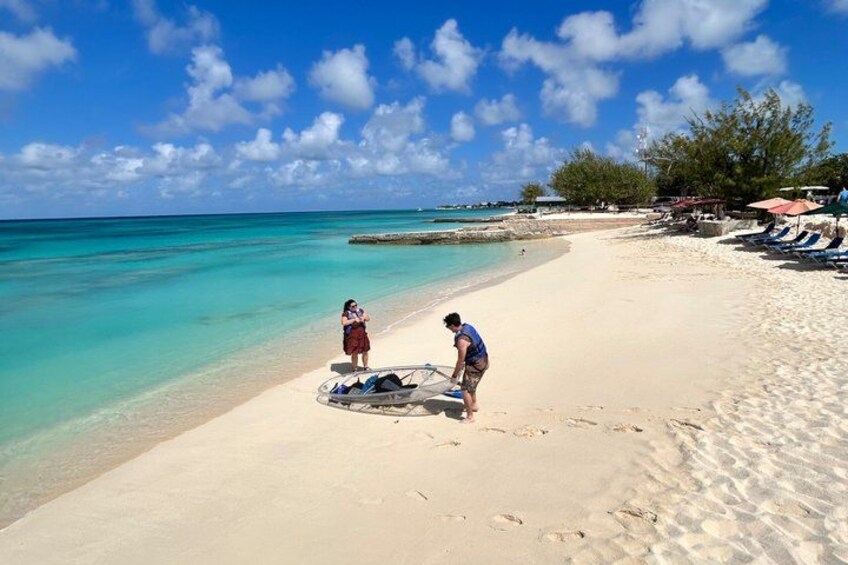 A beach with clear turquoise water, a sandy shore, and a few people near a boat. 5