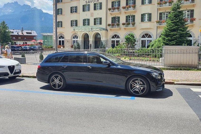 A black station wagon parked on a street with a building labeled 'SAVOIA' in the background. 2