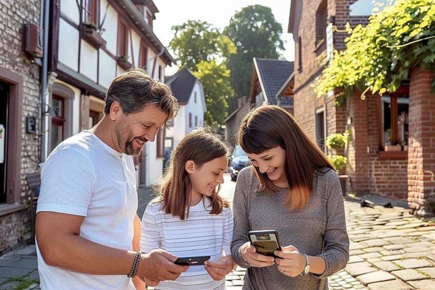 Drei Personen stehen auf einem Kopfsteinpflasterweg und betrachten ein Smartphone. 1