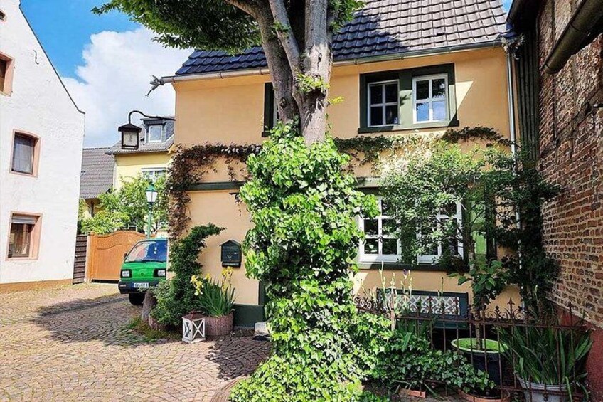 Ein gelbes Haus mit einer Ziegelwand, einem Baum davor und einem grünen Auto auf der Auffahrt. 4