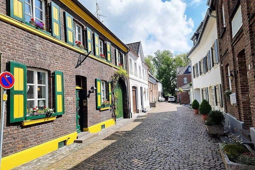 Eine Kopfsteinpflasterstraße gesäumt von bunten Gebäuden, ein Verbotsschild und ein klarer, blauer Himmel. 3