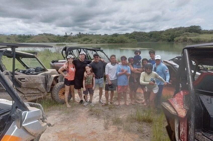 A group of people posing in front of off-road vehicles by a lake. 2