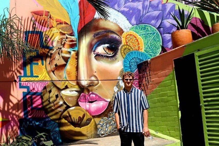 Et farverigt mural med geometriske mønstre, en person foran det, og en grøn murstensvæg. 4