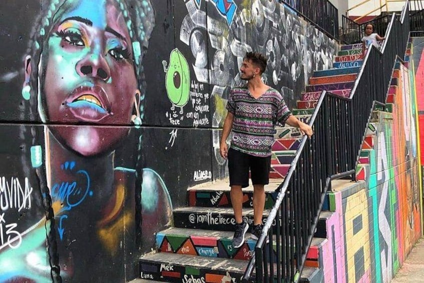 En person som går uppför en trappa där väggarna är prydda med färgstark graffiti. 1