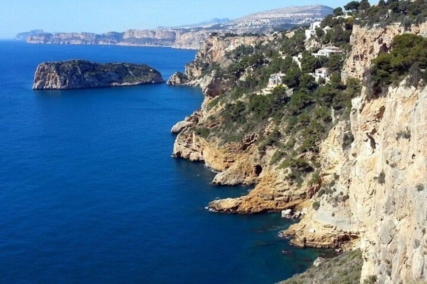 A coastal landscape with cliffs, a small island, and buildings on the hillside. 5