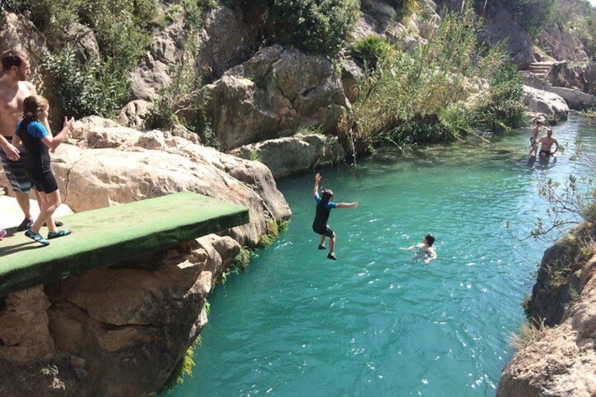 A rocky riverbank with people swimming and jumping into the water. 4