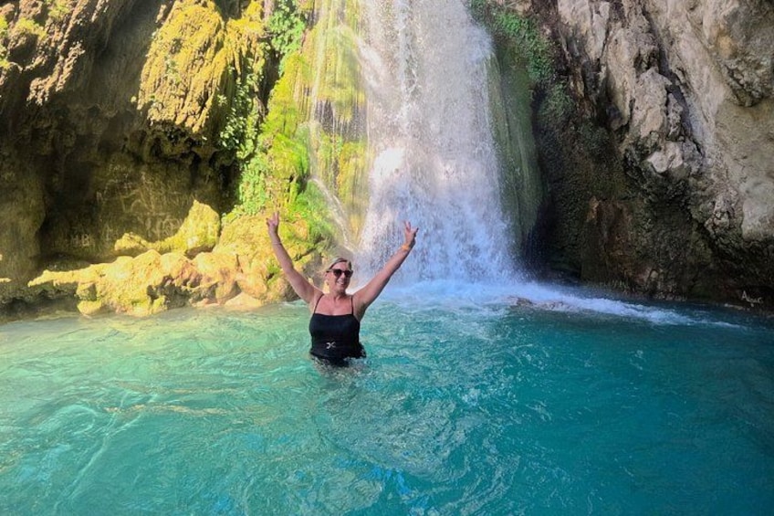 A person standing in clear water with a waterfall in the background. 1