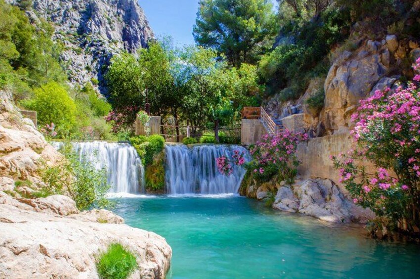 A waterfall cascading into a turquoise pool surrounded by rocky terrain and lush greenery. 3