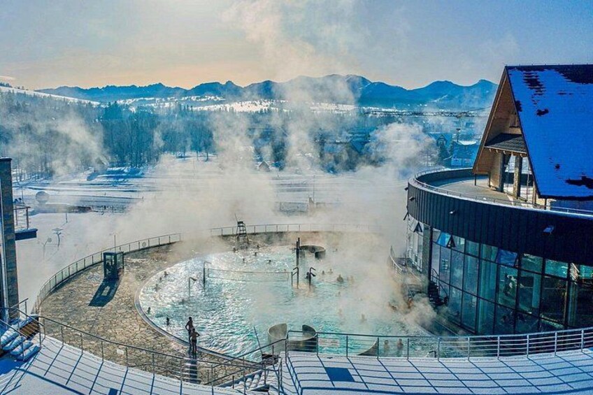 A geothermal spa with steam rising, surrounded by snow-covered mountains. 3