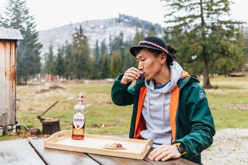 A person sitting at a wooden table outdoors with a bottle of Soplex vodka and a plate of food. 2