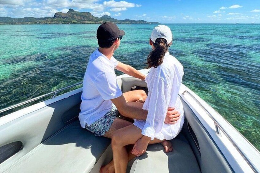 Deux personnes à bord d’un bateau sur une eau turquoise et limpide, avec un paysage montagneux en arrière-plan. 1