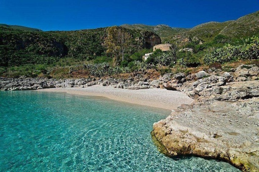 Eine Küstenlandschaft mit klarem türkisblauem Wasser, einem Sandstrand, Felsformationen und grünen Hügeln im Hintergrund. 4