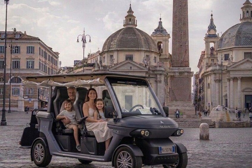 Een zwarte cabrio met vier passagiers op een historisch stadsplein. 4