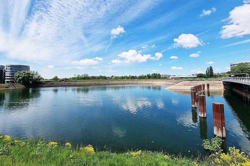A calm river with a bridge, greenery, and buildings in the background. 3