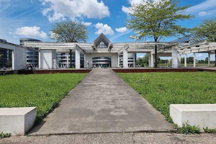 A modern building with a central entrance, surrounded by a green lawn and concrete pathways. 5