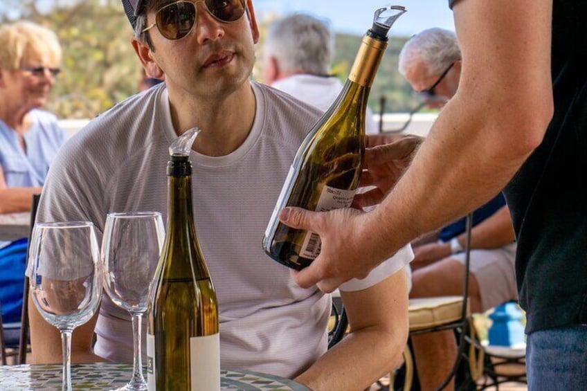 A person pouring wine into a glass at a table with other empty glasses and a wine bottle. 3