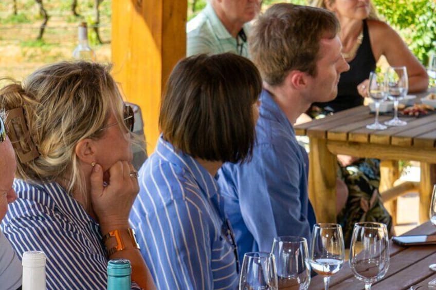 People sitting at a wooden table outdoors with wine glasses and bottles. 4