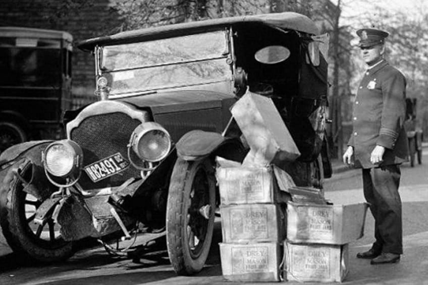 Un coche antiguo, un hombre con uniforme y una pila de cajas. 2