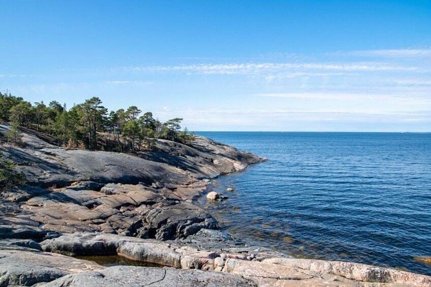 A rocky coastline with clear blue water, trees, and a distant horizon. 2