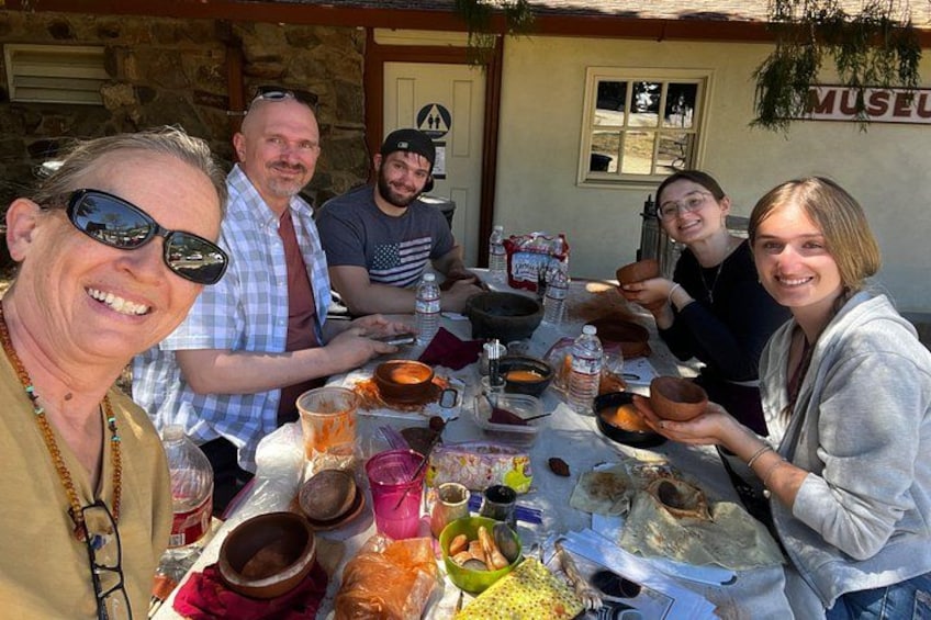 A group of people sitting at an outdoor table with various food items and drinks. 2