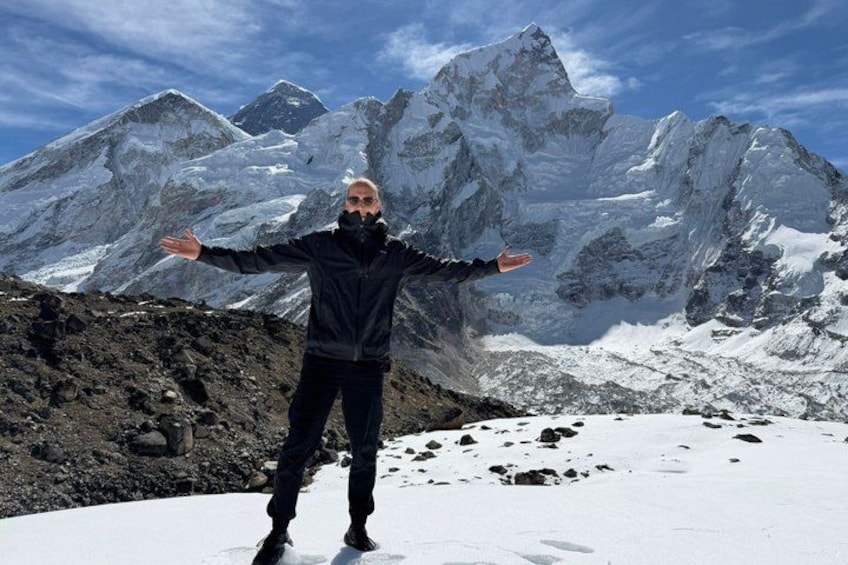 A person standing on a snow-covered peak with arms outstretched, facing a mountain range. 3