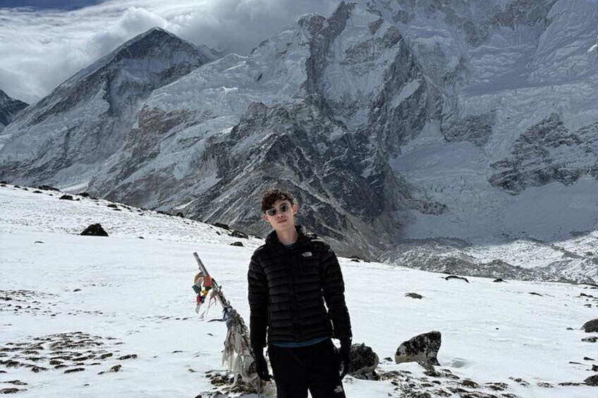 A person standing on a snow-covered mountain with a rocky landscape and a mountain peak in the background. 2