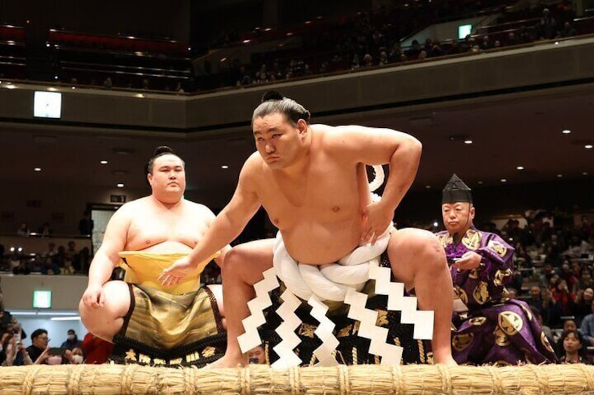 A sumo wrestling match with two wrestlers and a referee. 1