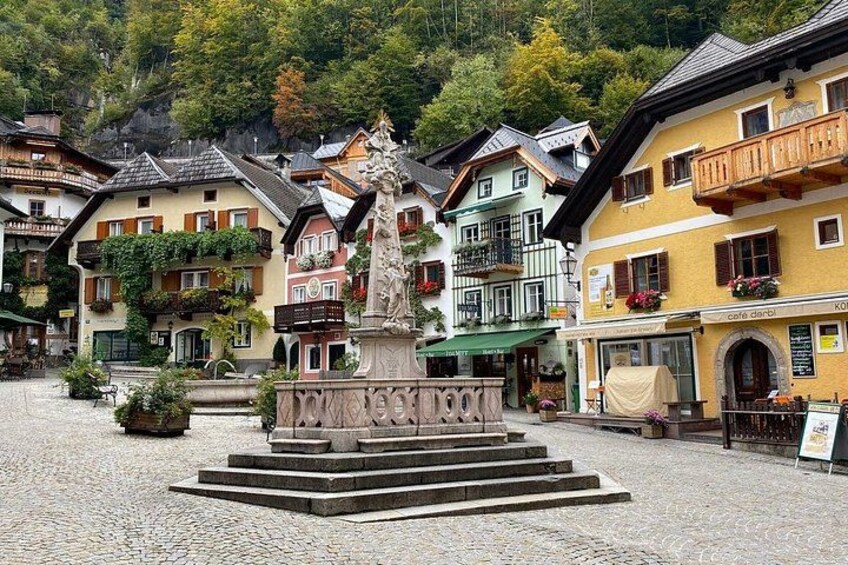 A cobblestone square with a central fountain, surrounded by colorful traditional buildings with balconies and flower boxes. 2