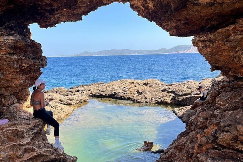 A rocky cave opening to a clear blue sea, with a person sitting inside. 4