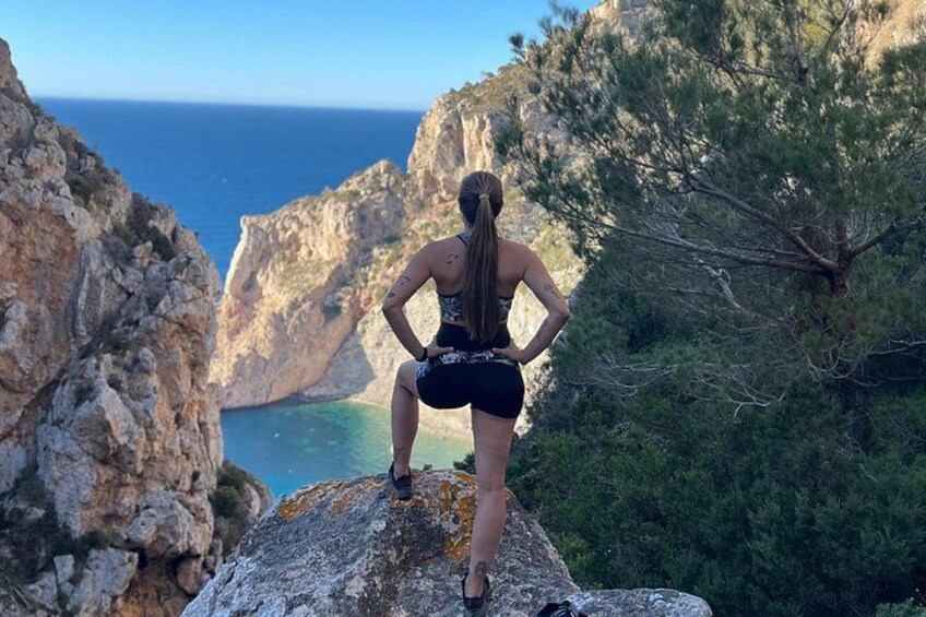 Una persona de pie sobre un saliente rocoso, con vistas a un paisaje costero con acantilados y árboles. 1