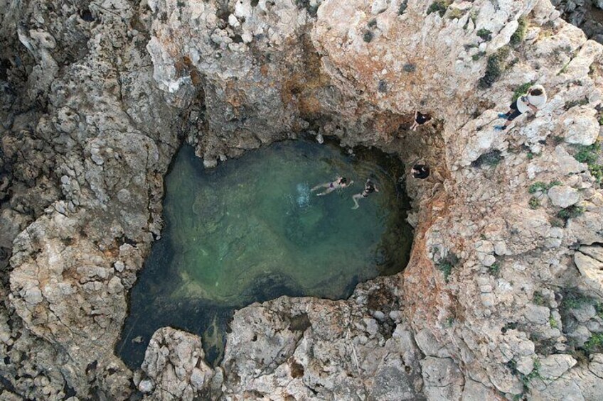 A rocky terrain with a small body of water and people swimming. 3