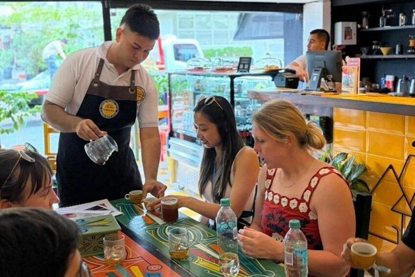 A coffee shop with a colorful table, a barista preparing drinks, and customers seated. 4