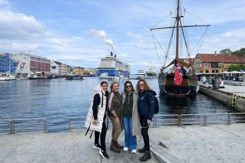 A group of people standing by a waterfront with a tall ship and cruise ships in the background. 1
