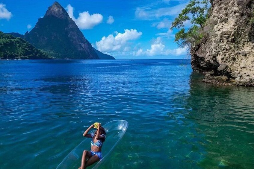 A person lying on a surfboard in clear blue water with a mountain in the background. 1