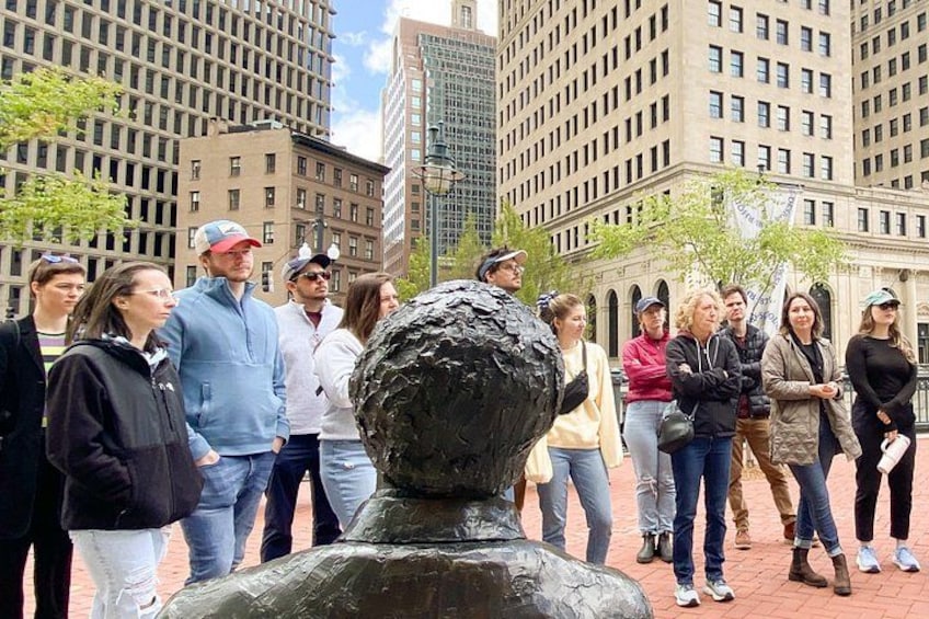 A group of people standing in front of a sculpture in an urban setting with tall buildings in the background. 2