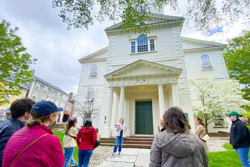 A group of people standing in front of a white building with columns and a green door. 3