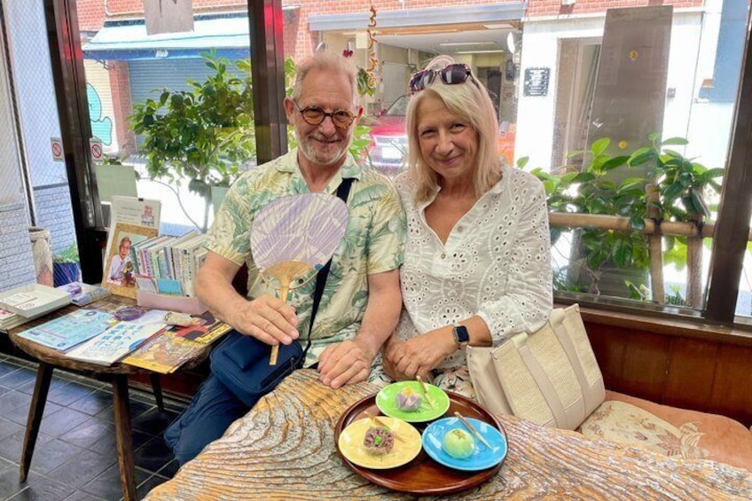 Two people seated at a table with a plate of food and a fan. 5