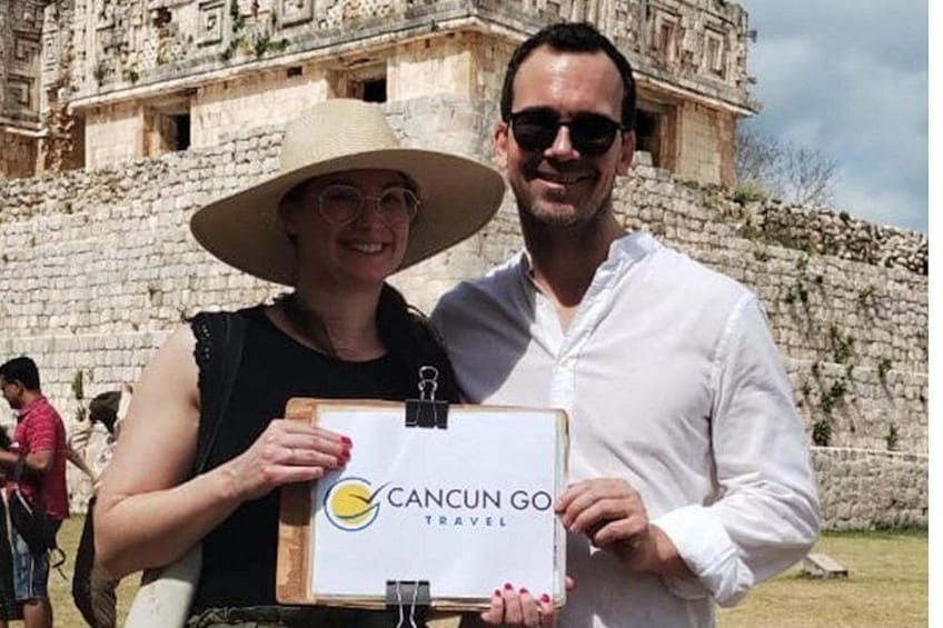 Eine Person hält ein Schild mit dem Text 'Cancun Go Travel' vor einer Steinstruktur. 2